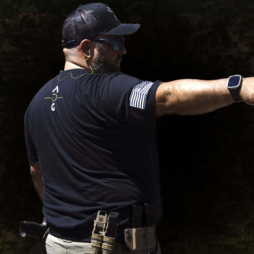 Man wearing an American operator t-shirt, pointing with one hand and showcasing a professional tactical style.